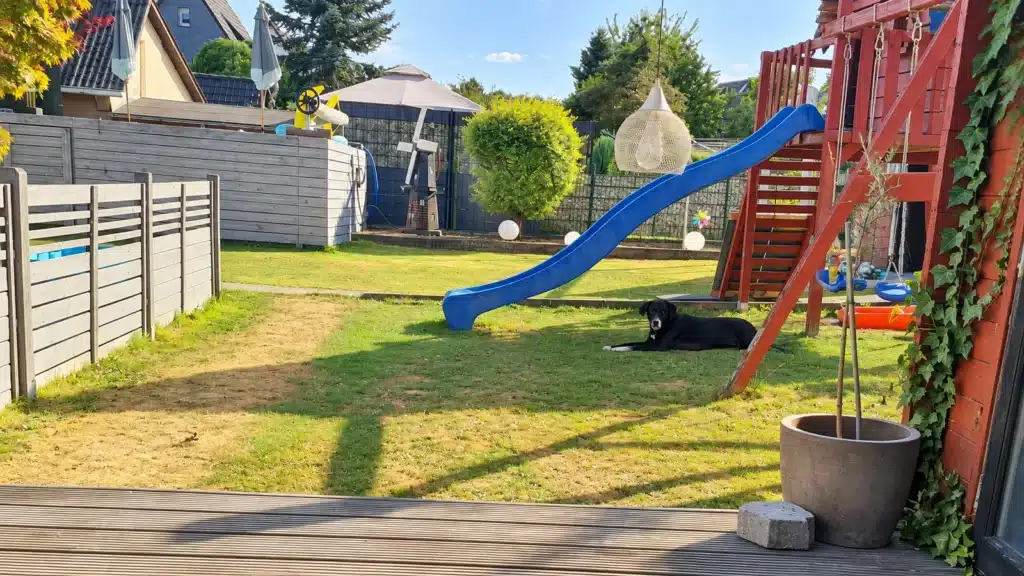 Eingezäunter Garten mit Spielturm und Rutsche, Familienhündin Nala liegt im Gras